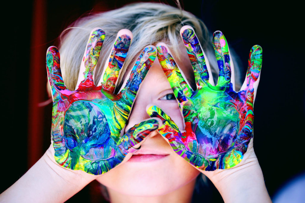 little child putting painted hands over his face to hide face